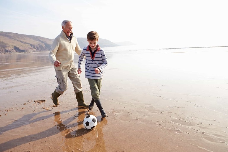 Posture and sciatica. How to improve your fitness with correct posture. Older man enjoys playing football on beach with child.
